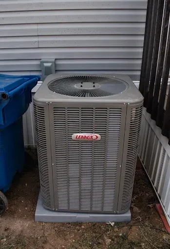 Lennox air conditioner unit, gray, outside a building, next to a blue trash bin.