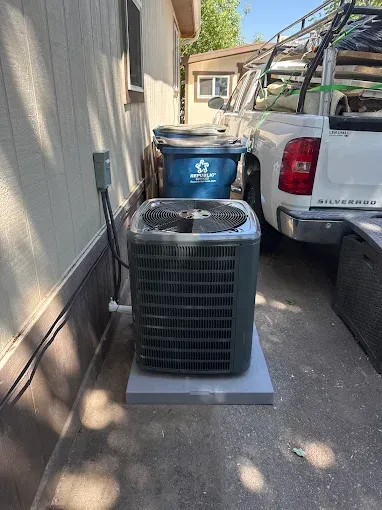 AC unit on a concrete pad next to a wall, trash bin, and truck.