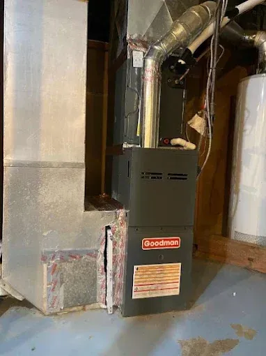 A Goodman furnace in a basement setting with ductwork and a water heater visible.