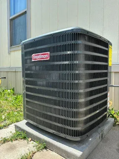 Goodman air conditioning unit on a concrete pad near a house.
