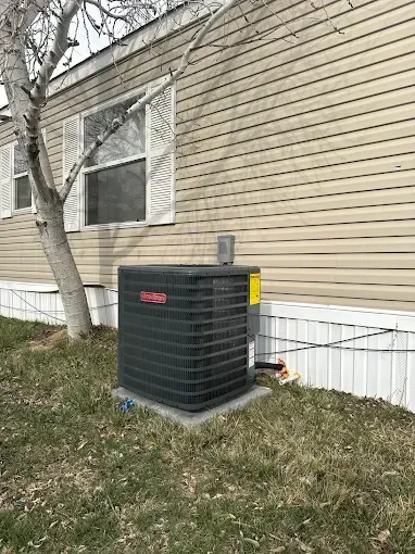 Air conditioning unit next to a light-colored mobile home, situated on a concrete pad in a grassy yard.