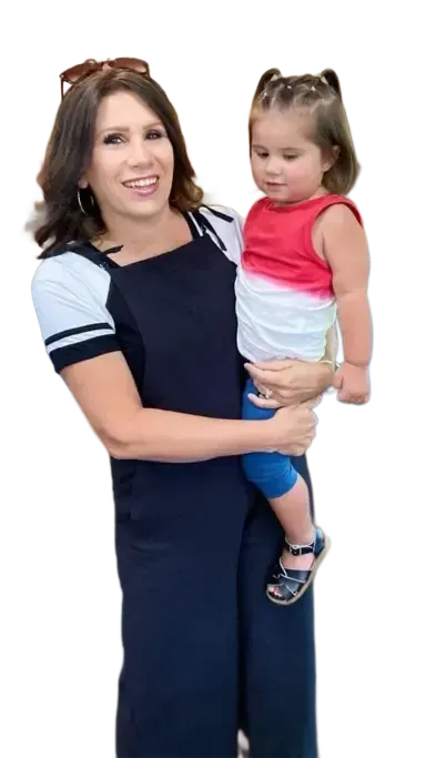 Woman in jumpsuit holds a young child wearing red, white, and blue shirt and blue leggings.