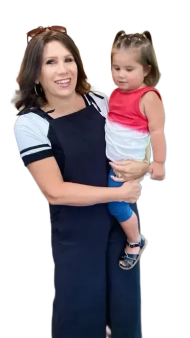 Woman in jumpsuit holds a young child wearing red, white, and blue shirt and blue leggings.