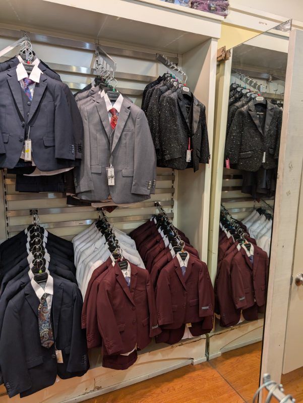 Suits hanging in a clothing store, arranged by color.