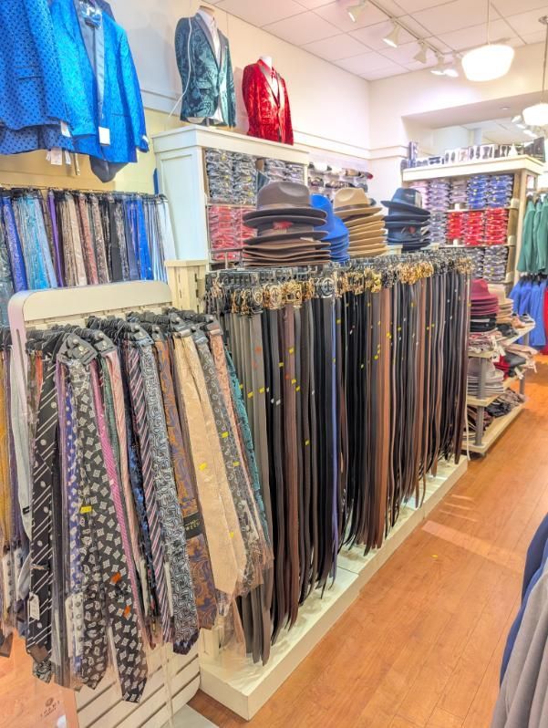 Clothing store interior with ties, belts, hats, and jackets on display.