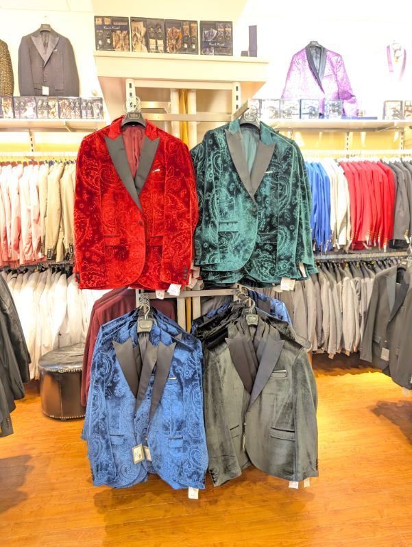 Men's velvet tuxedo jackets in red, green, blue, and black displayed in a clothing store.