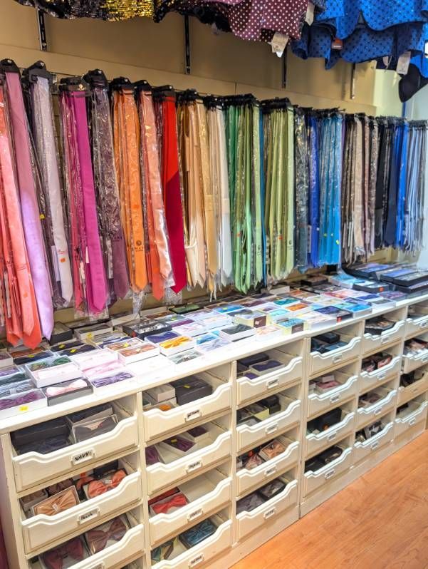 Ties of various colors hanging above drawers of folded ties in a store.
