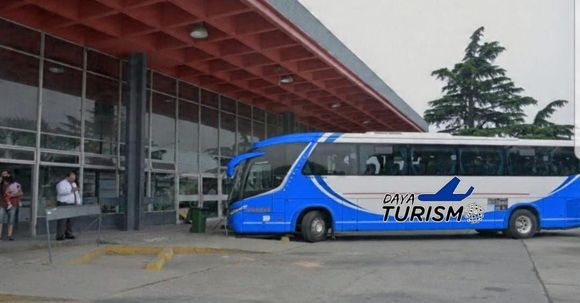 Un autobús turístico azul estaba estacionado frente a un edificio con fachada de cristal, bajo una entrada cubierta.