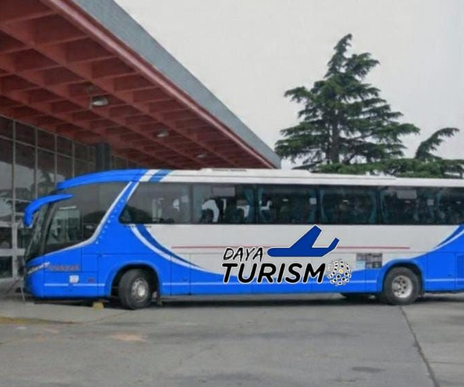 Un autobús turístico azul y blanco estacionado junto a un edificio de techo rojo.