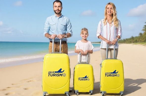 Familia con maletas amarillas en una playa soleada, sonriendo junto al océano.