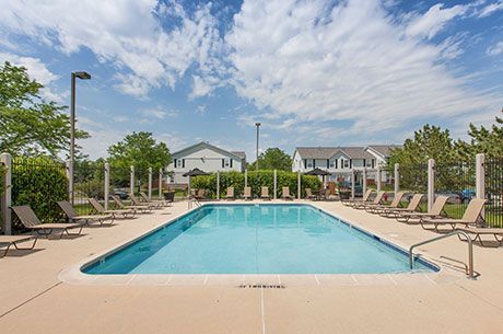 a large swimming pool surrounded by chairs and umbrellas in front of a building .