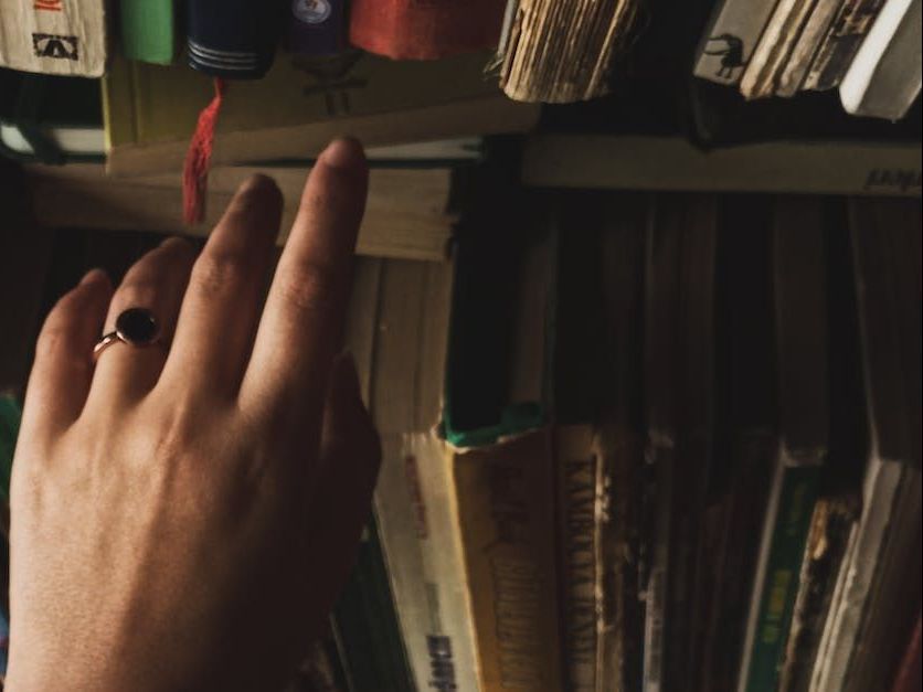 a person wearing a ring is reaching for a book on a shelf