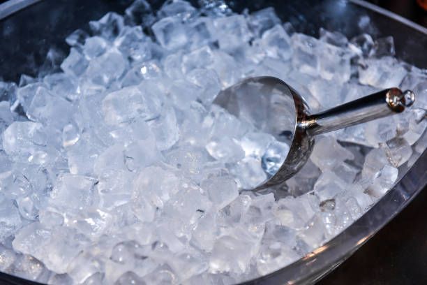Metal scoop resting in a clear bowl filled with ice cubes for cooling and beverage service.