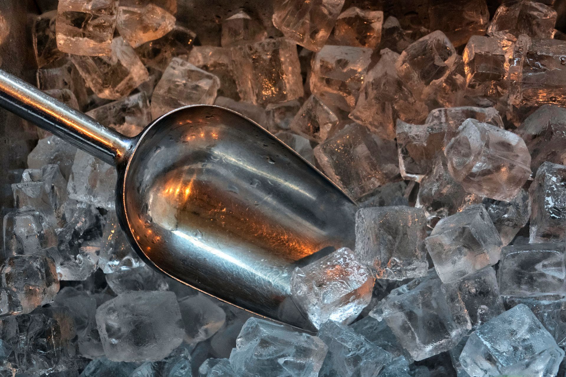 High angle and close up view of ice cubes and scoop in a storage.