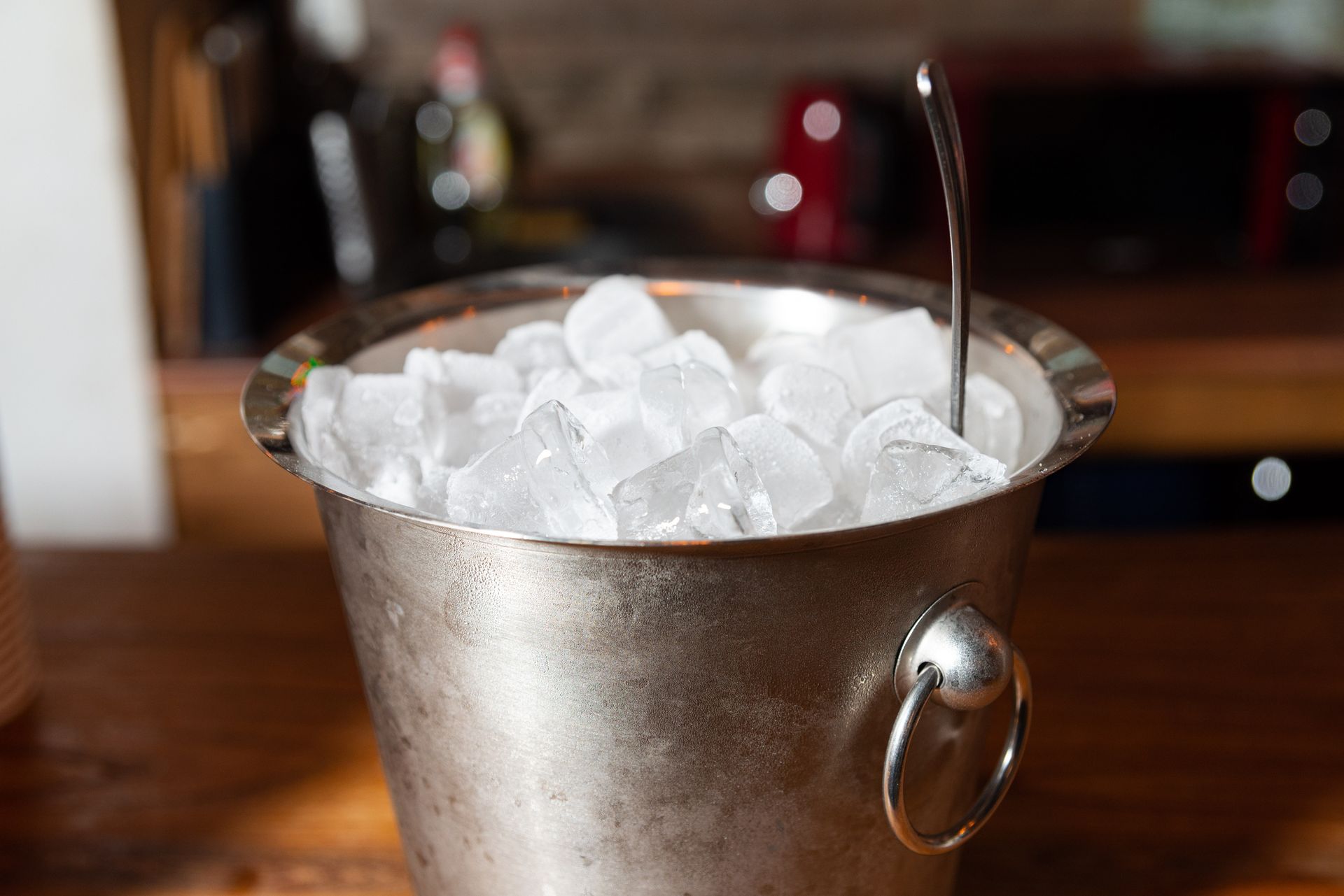 A metal bucket filled with ice cubes sits on a wooden countertop. A metal bucket filled with ice cubes sits on a wooden countertop.
