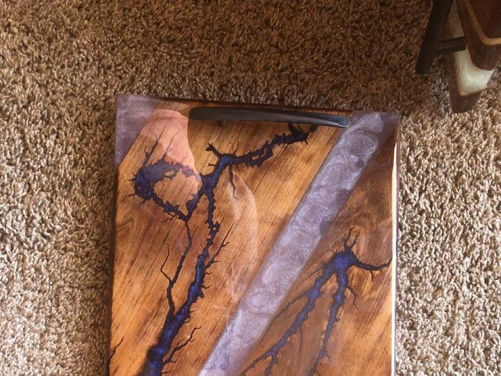 A wooden cutting board with purple resin on it is sitting on a carpet.
