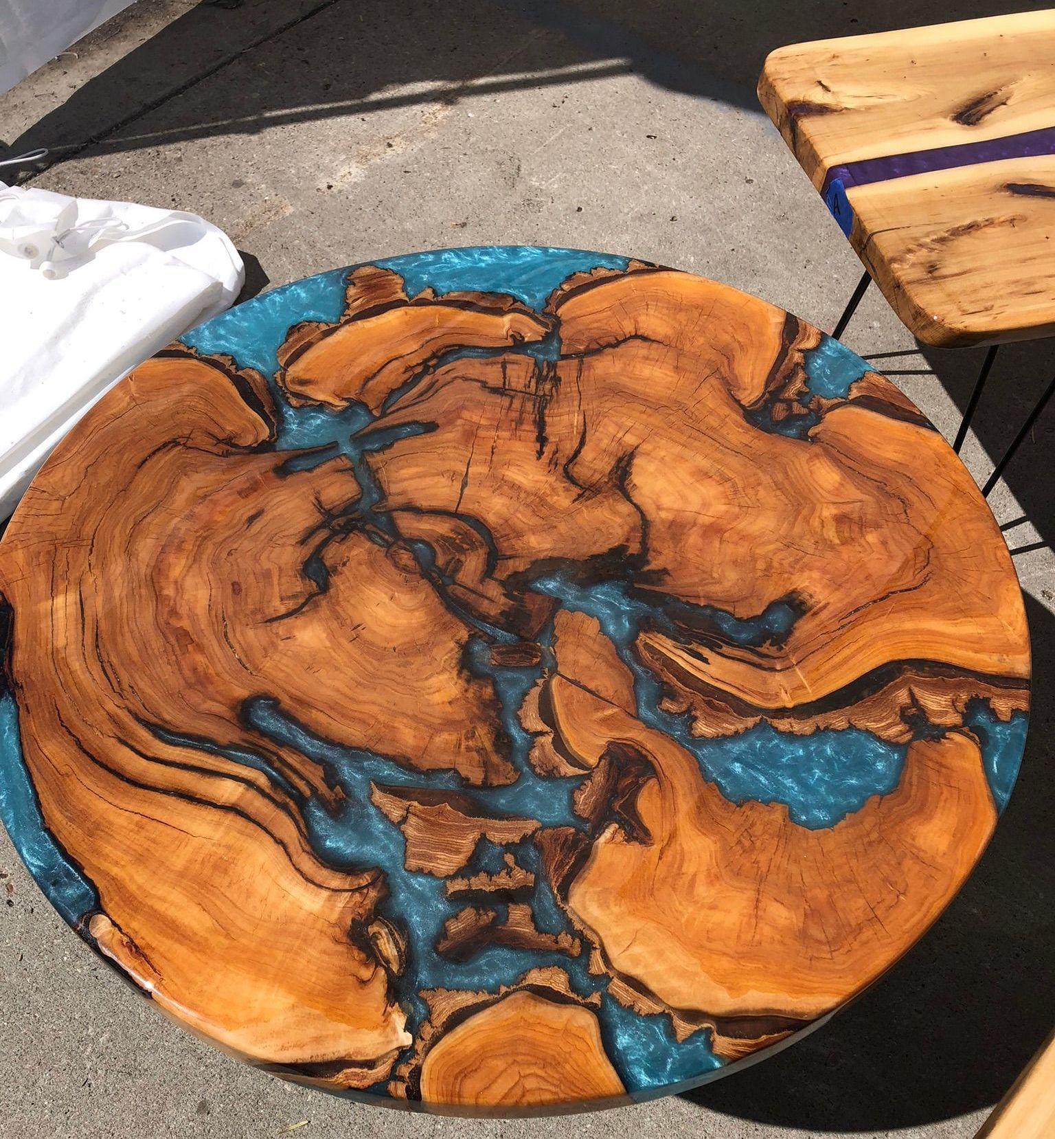 A wooden table with a blue resin top is sitting on the ground.