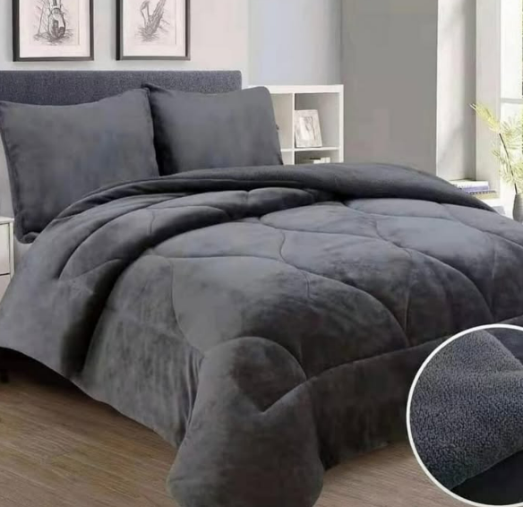 Una cama con un edredón gris y almohadas en un dormitorio.