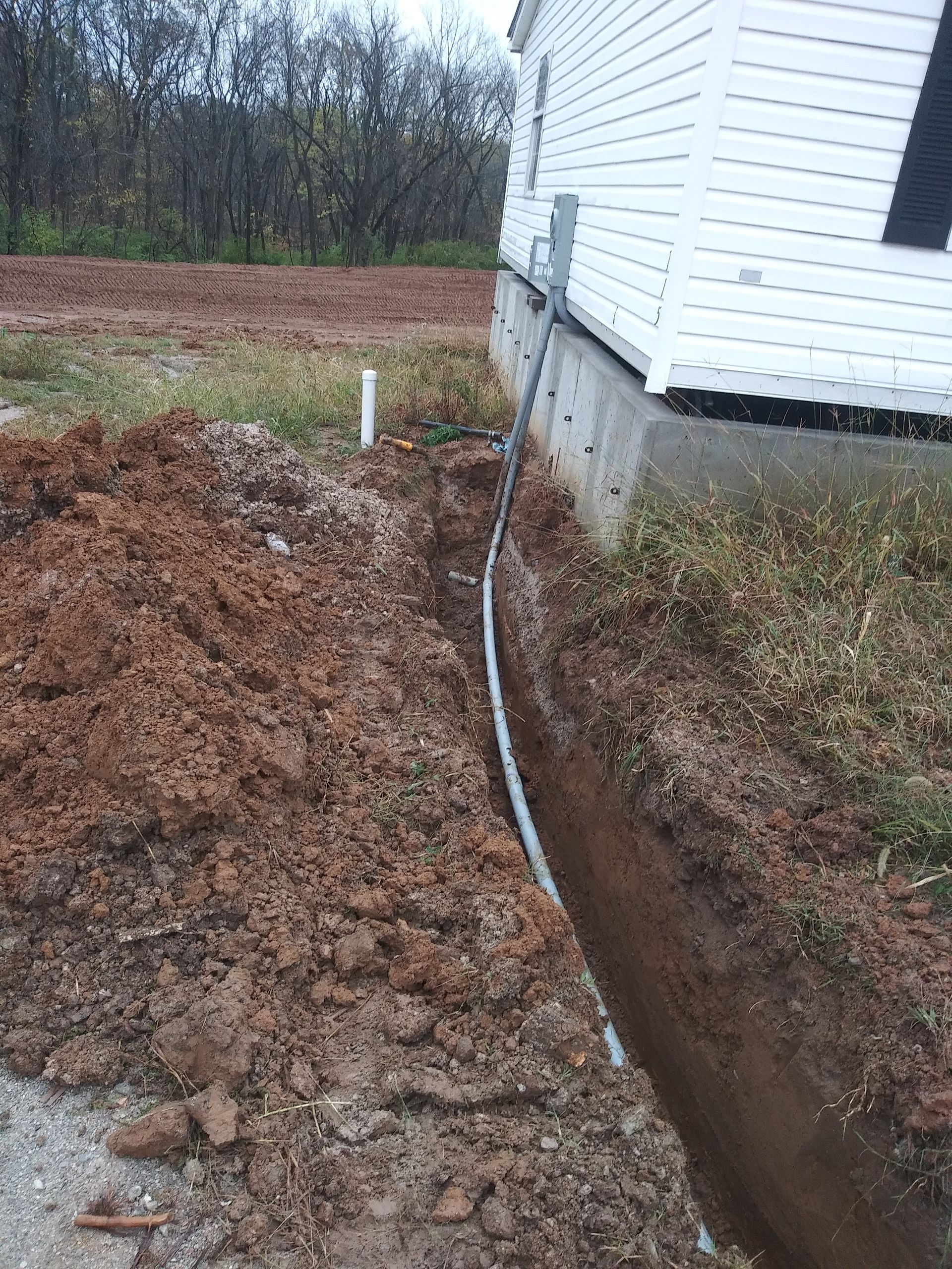 A Pipe Is Being Installed in The Dirt Next to A House | Winfield, MO | Excalibur Manufactured Housing Services LLC