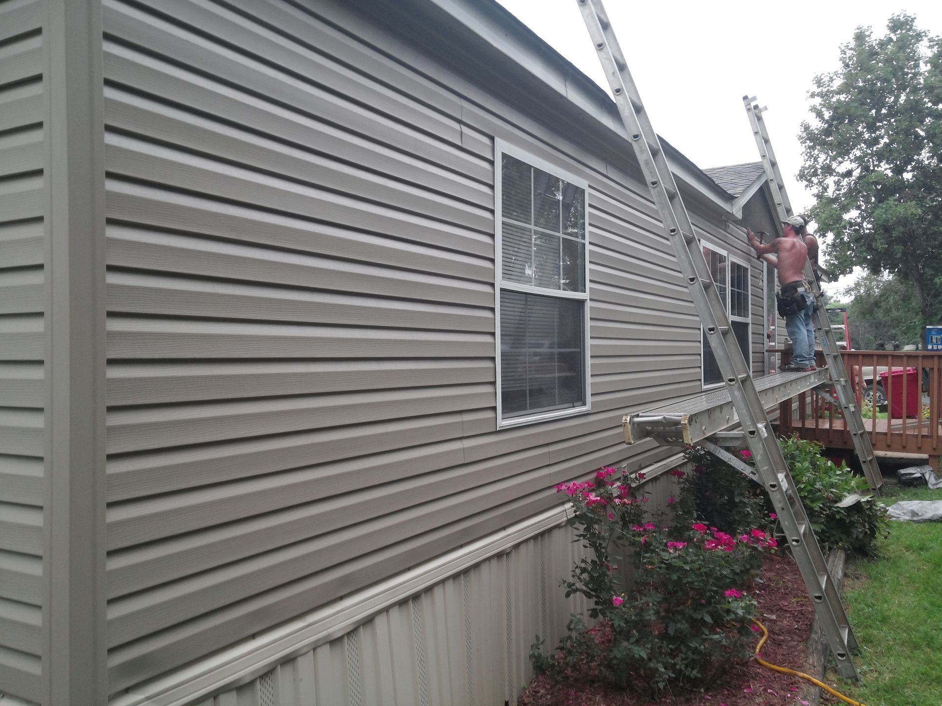 A Man Is Standing on A Ladder on The Side of A House | Winfield, MO | Excalibur Manufactured Housing Services LLC