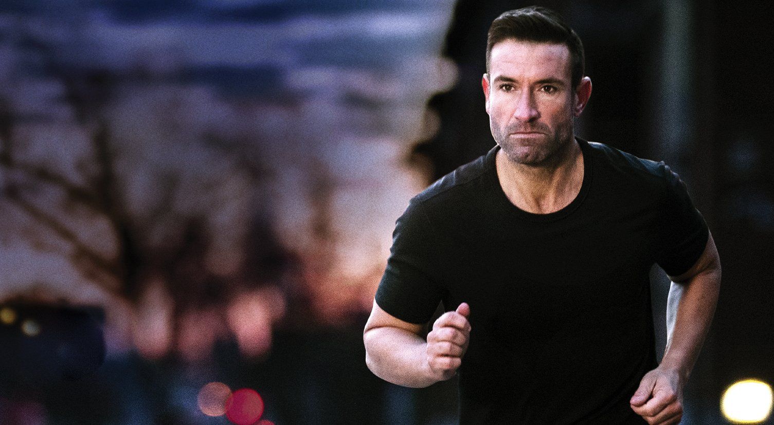 A man in a black shirt is running on a city street at night.