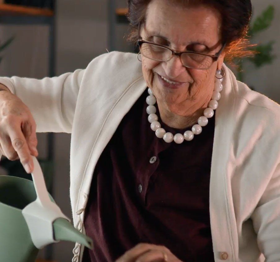 A woman wearing glasses and a pearl necklace is pouring something into a green pot