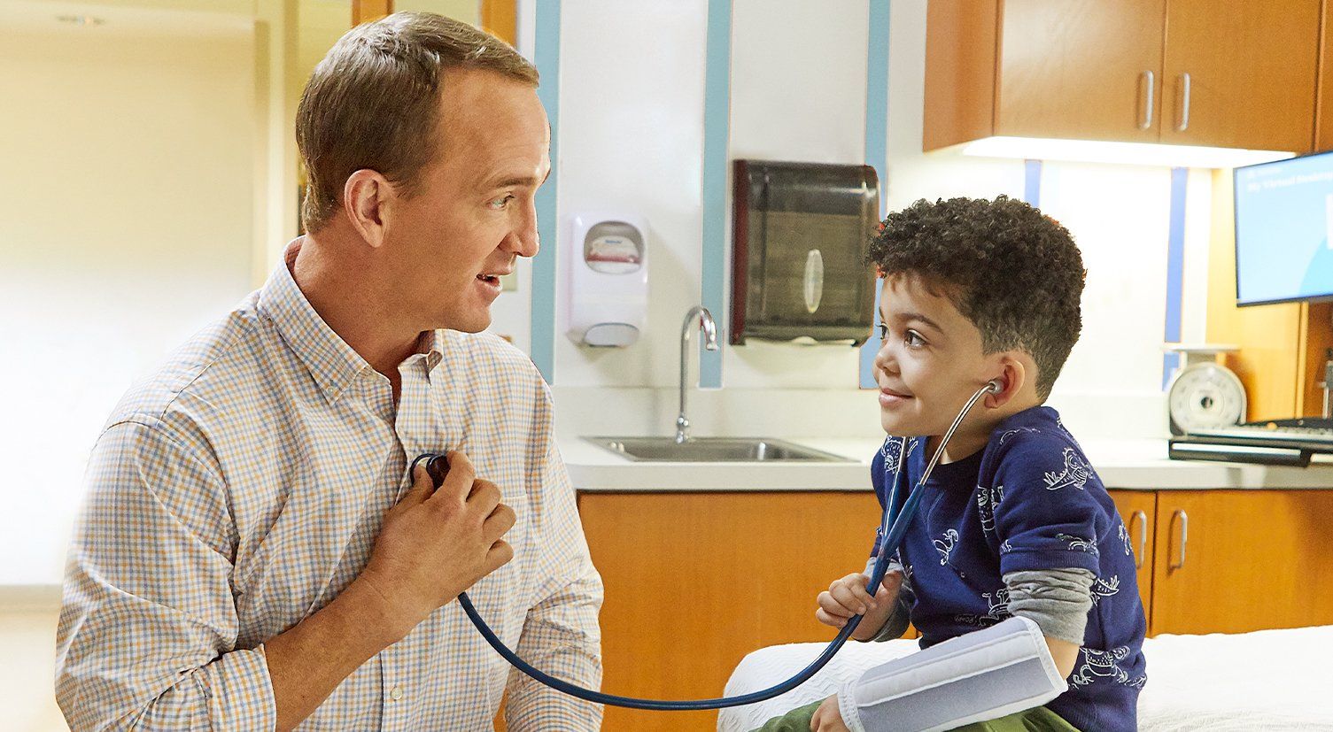 Peyton Manning is using a stethoscope to listen to a young boy 's heartbeat.