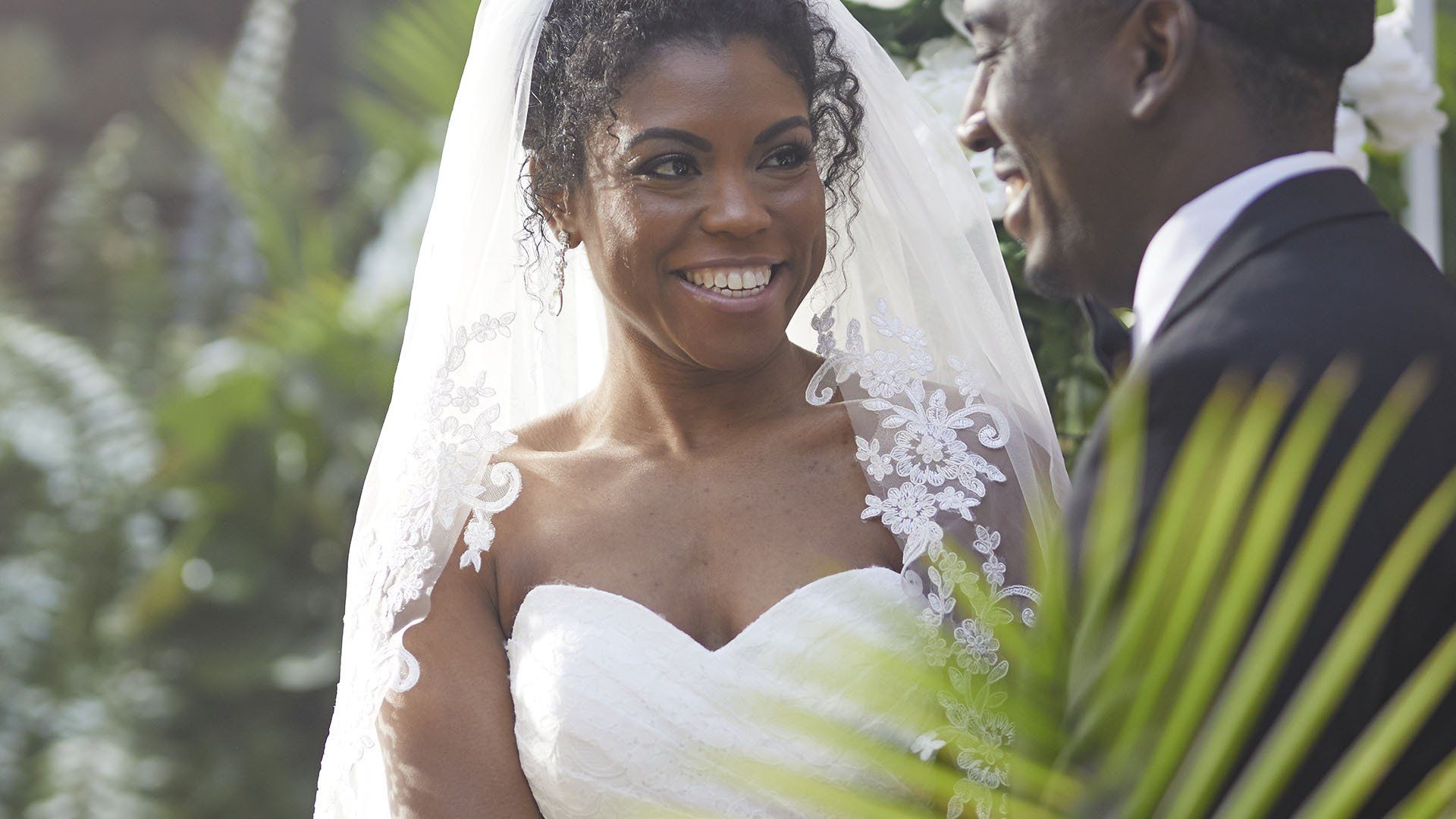 A bride and groom are smiling at each other during their wedding ceremony.