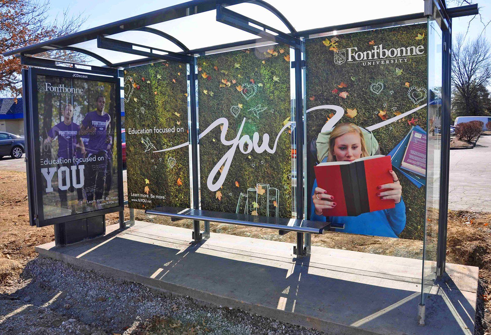 A bus stop with a poster of a girl reading a book.