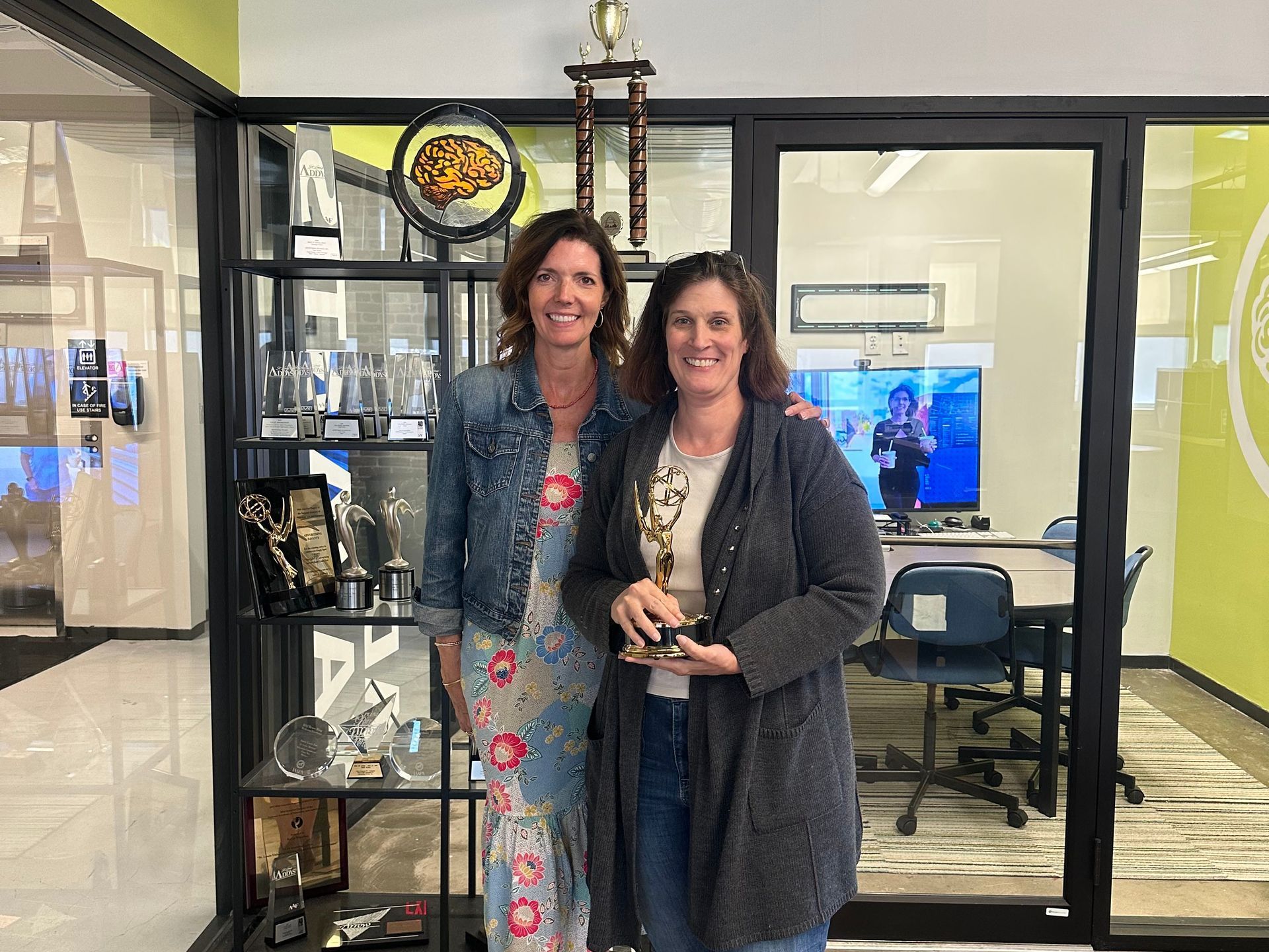 Two women are standing next to each other in a room holding trophies.