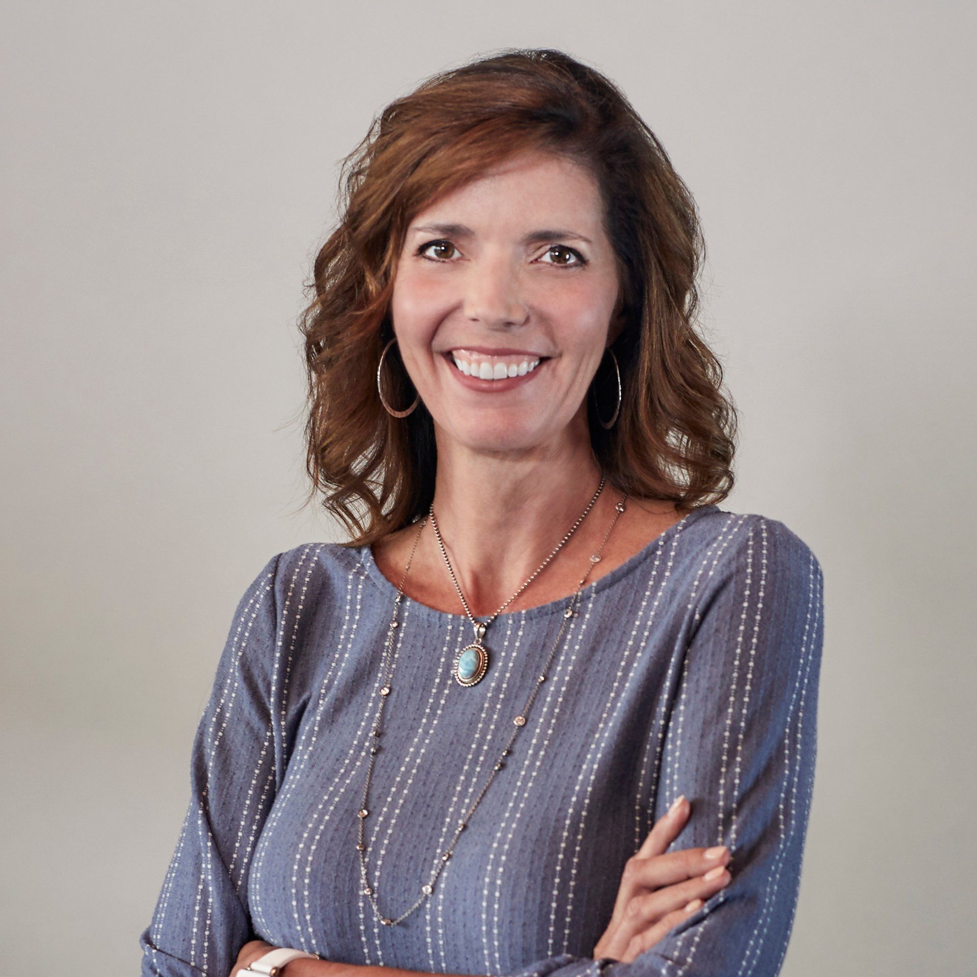 A woman in a blue striped shirt is smiling with her arms crossed