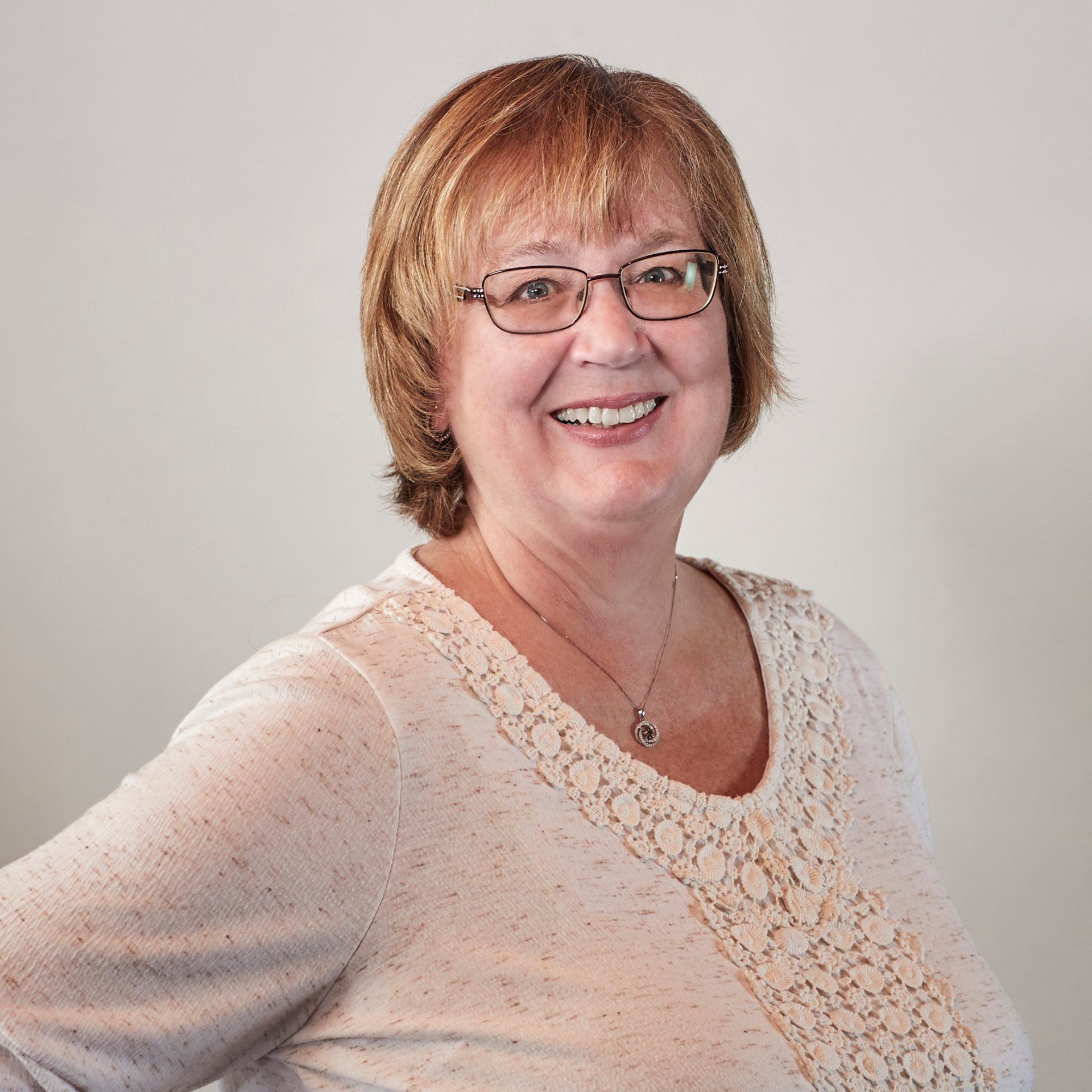 A woman wearing glasses and a white sweater smiles for the camera