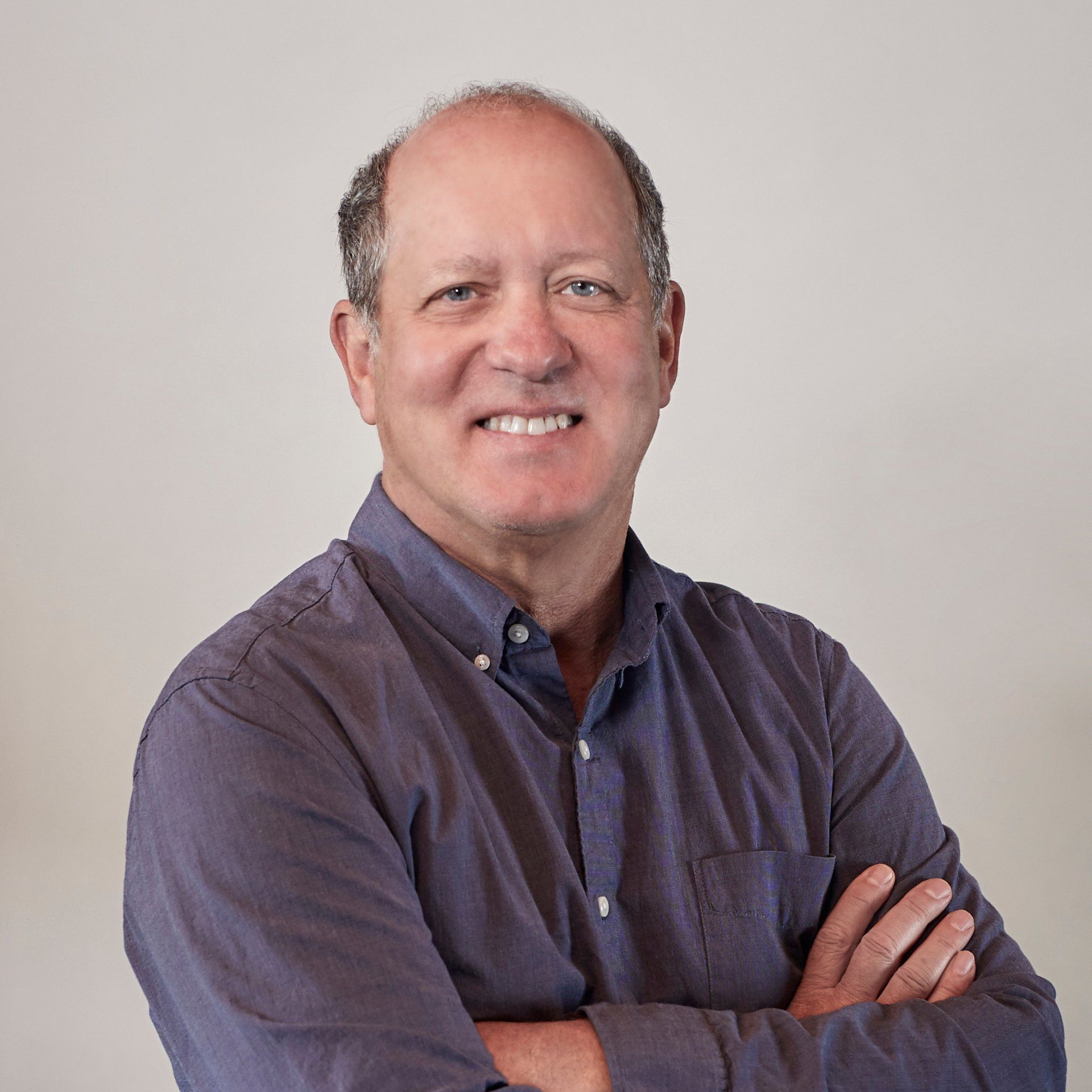 A man in a blue shirt is smiling with his arms crossed