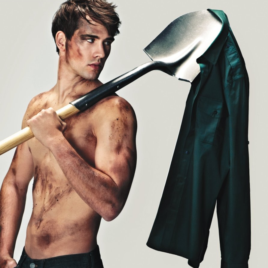 A shirtless man is holding a shovel over his shoulder