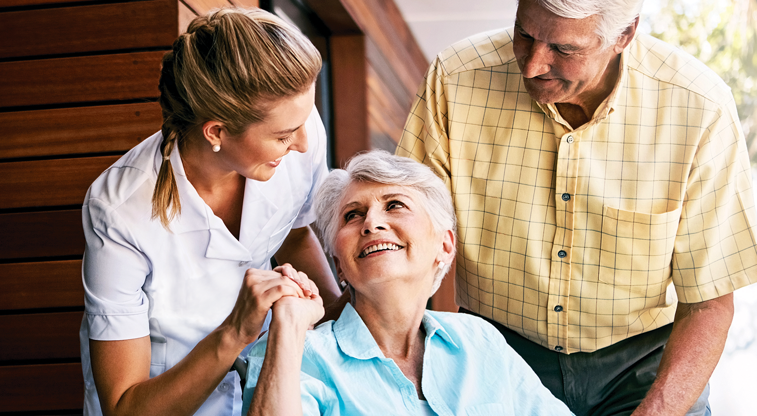 A nurse is holding the hand of an elderly woman while a man and woman look on.
