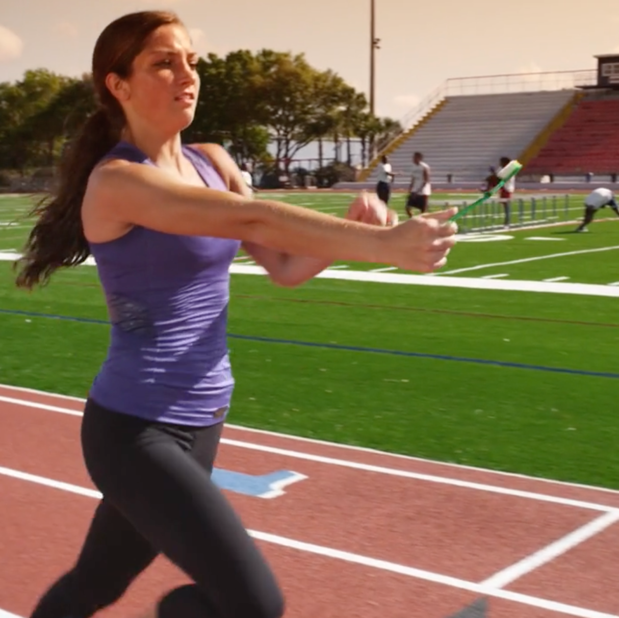 A woman in a purple tank top is running on a track