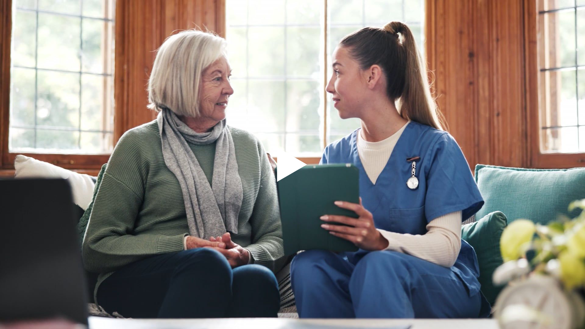 A nurse and resident siting on a couch talking.