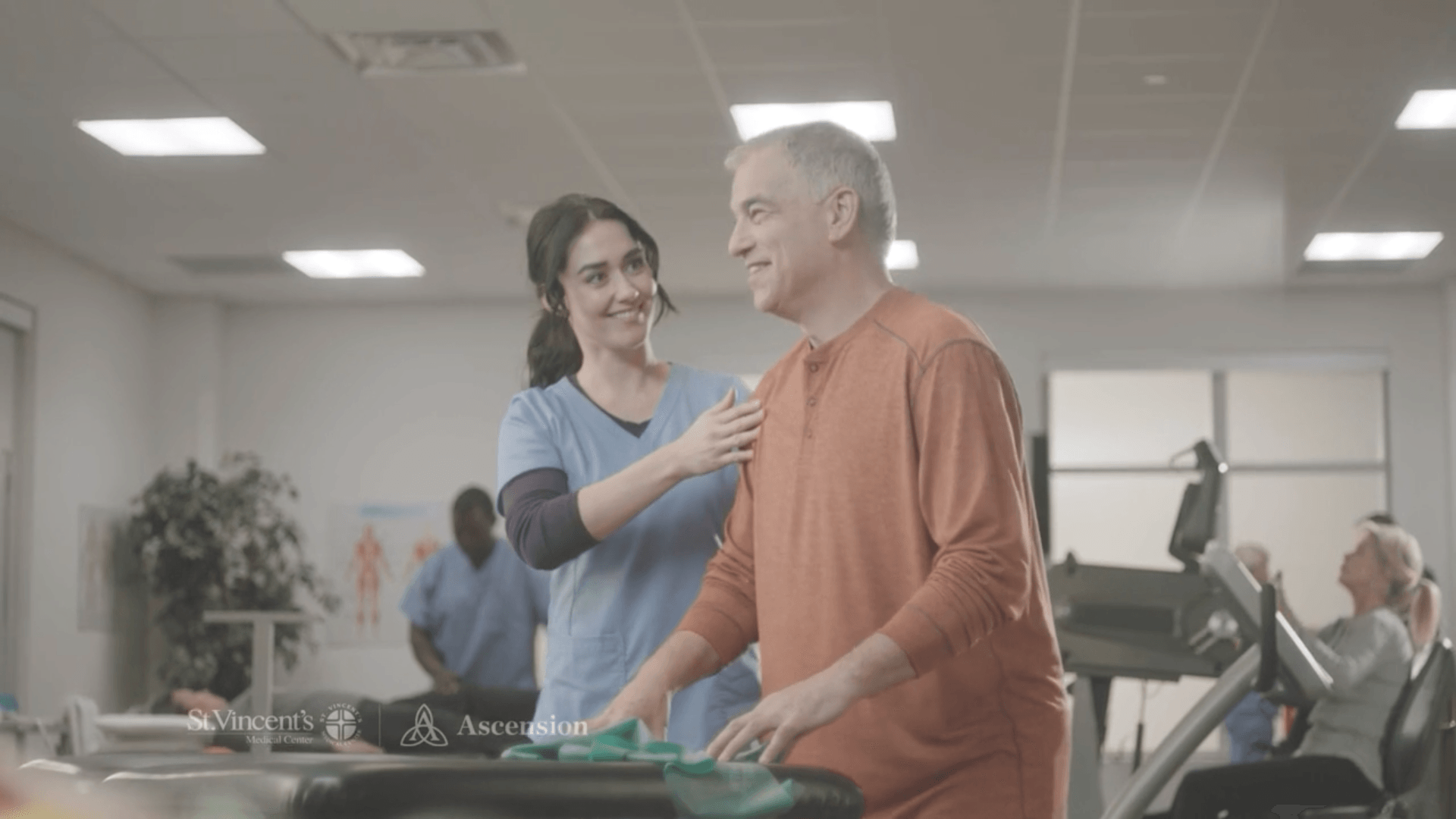 A woman is helping a man walk on a treadmill in a gym.