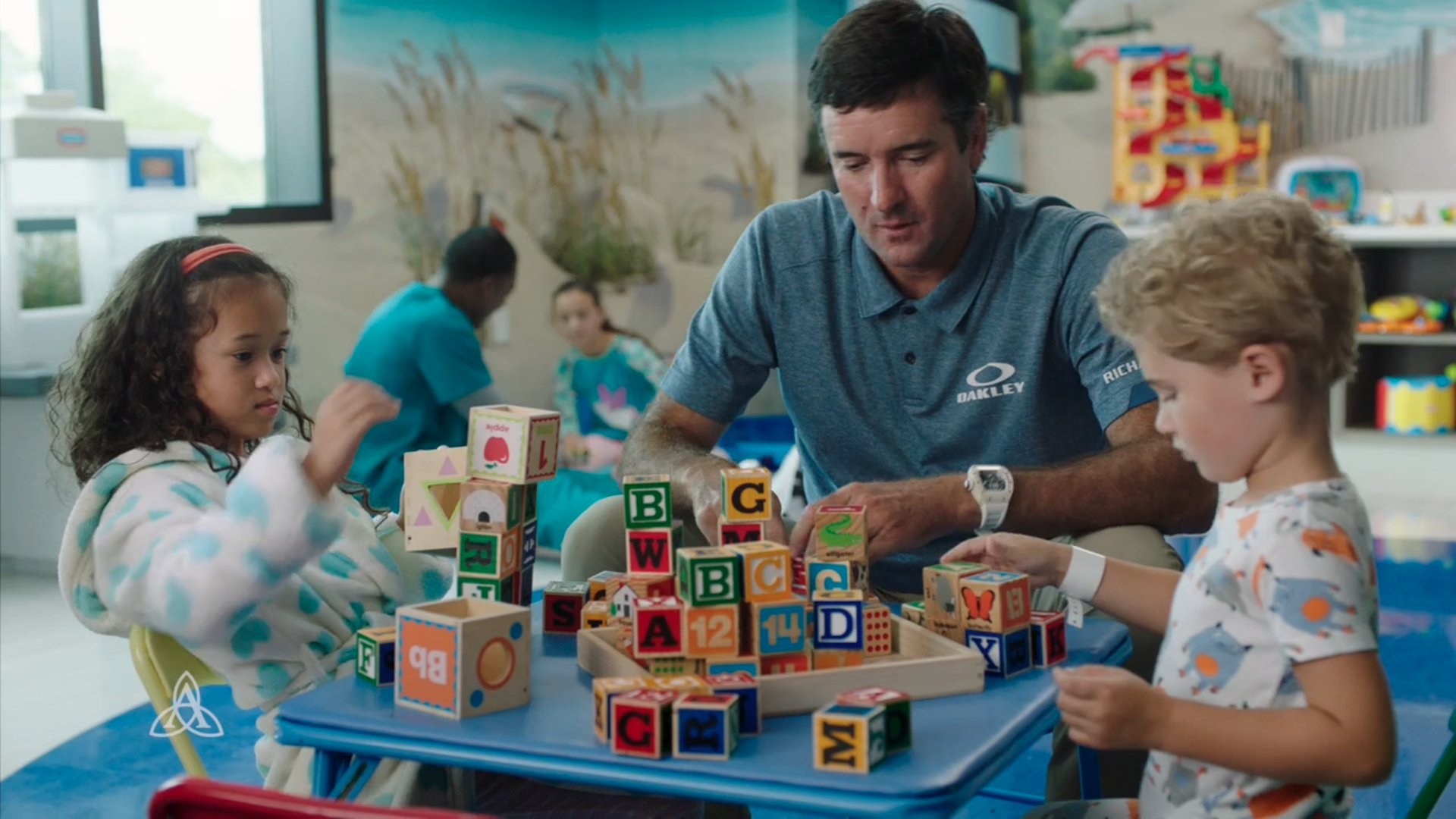 Bubba Watson and two children are playing with wooden blocks at a table.