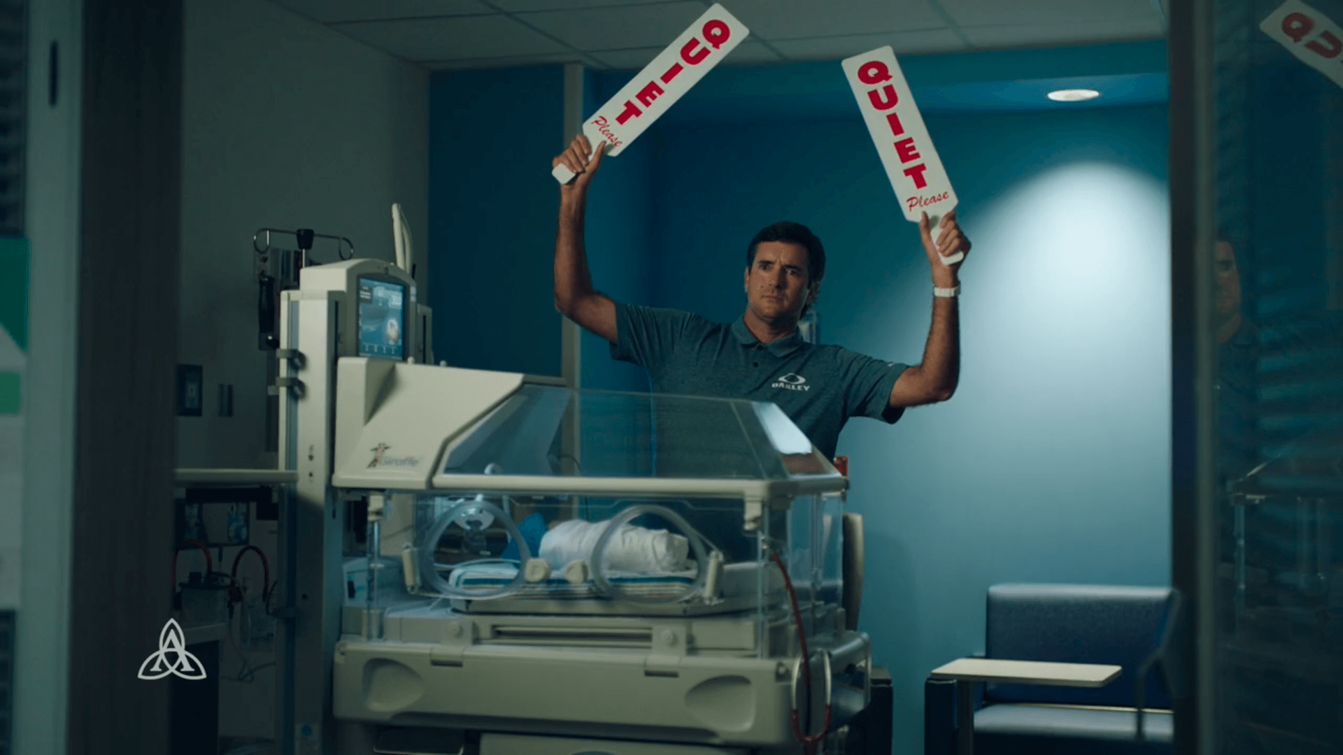 A man is holding a sign in front of an incubator in a hospital room.