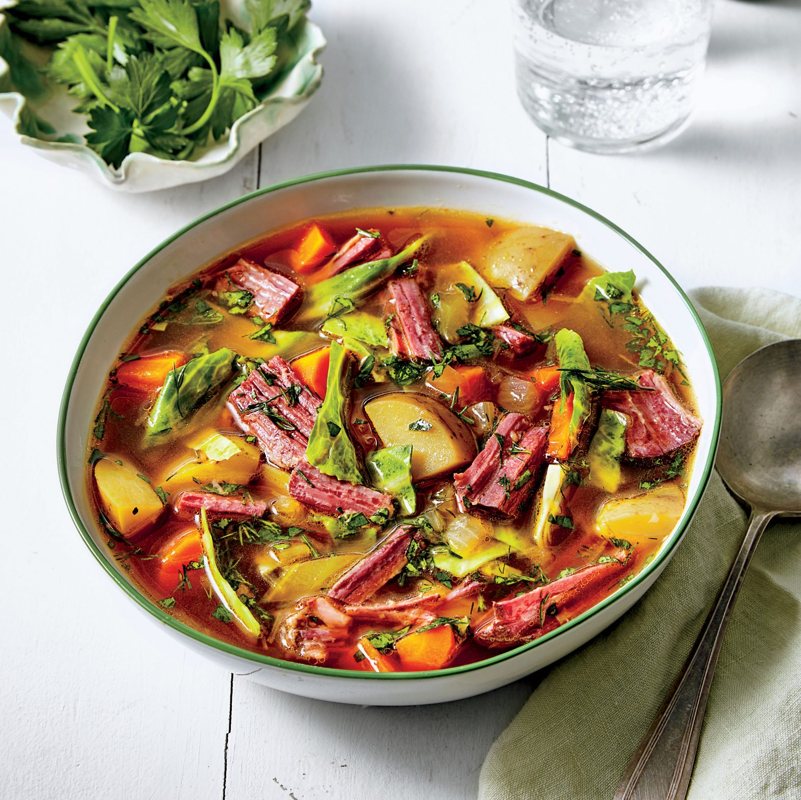 A bowl of soup with meat and vegetables next to a spoon