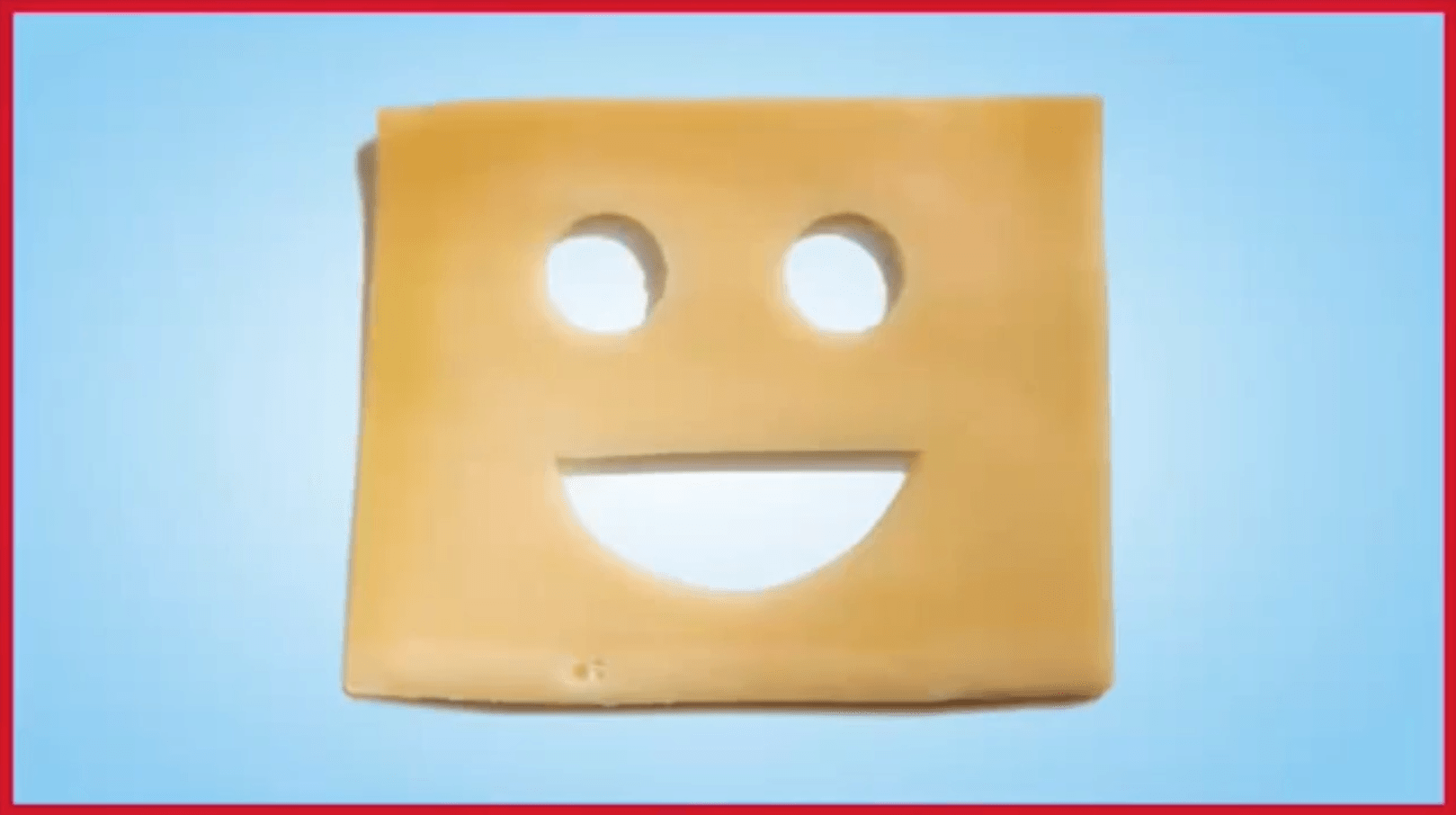 A piece of cheese with a smiley face cut out of it