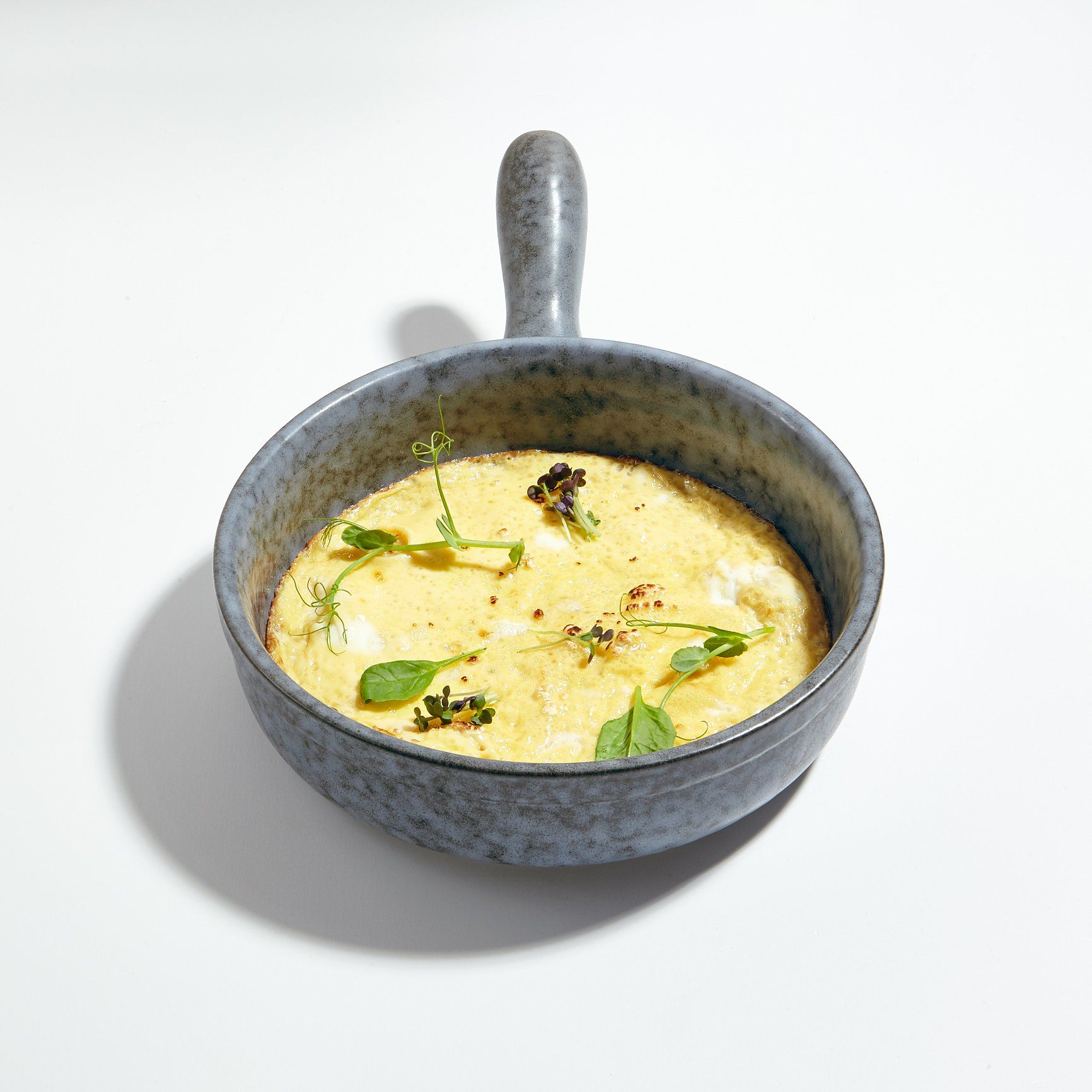A bowl of soup with a handle on a white surface.