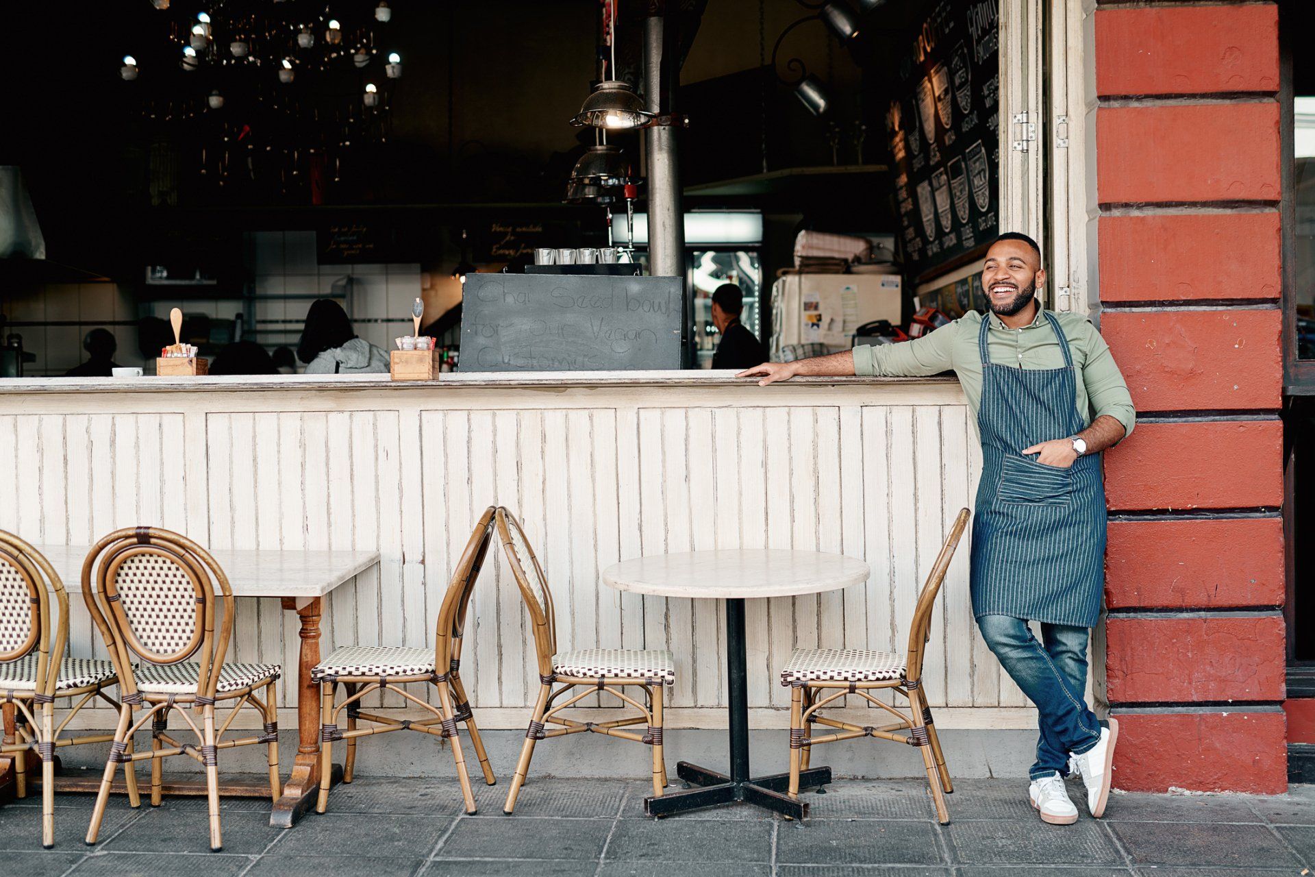 A man in an apron is leaning against the counter of a restaurant.