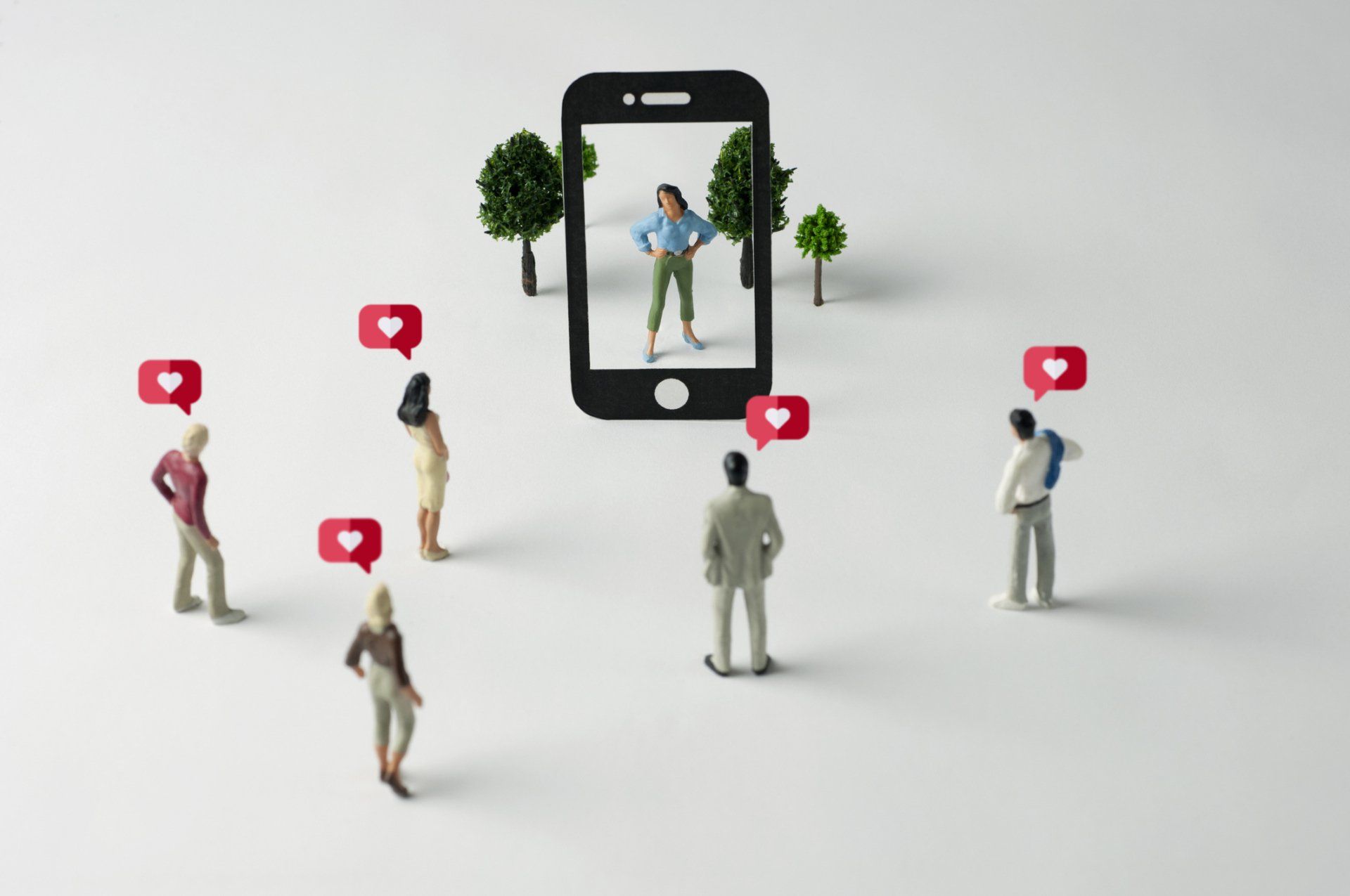 A group of miniature people standing around a cell phone.