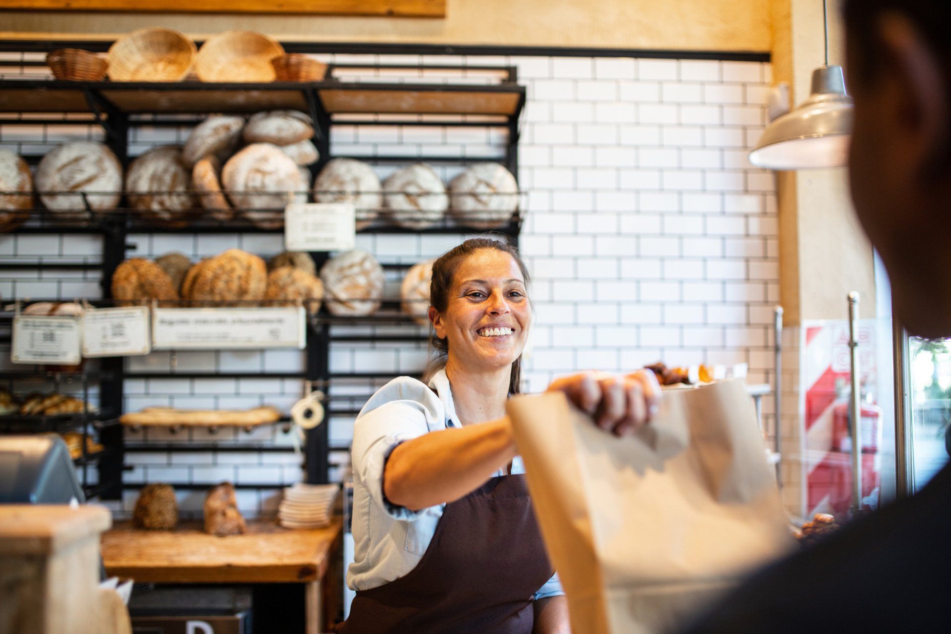 A woman is giving a bag to a man in a bakery.