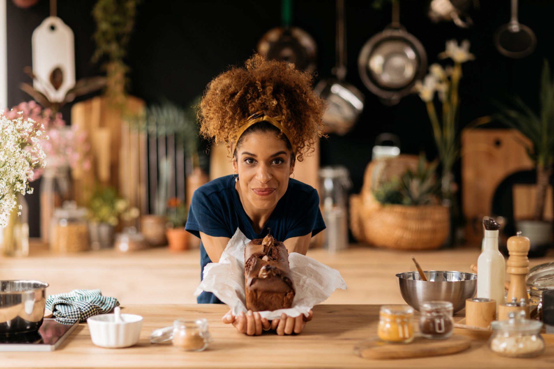 A woman is holding a loaf of cake in her hands in a kitchen.