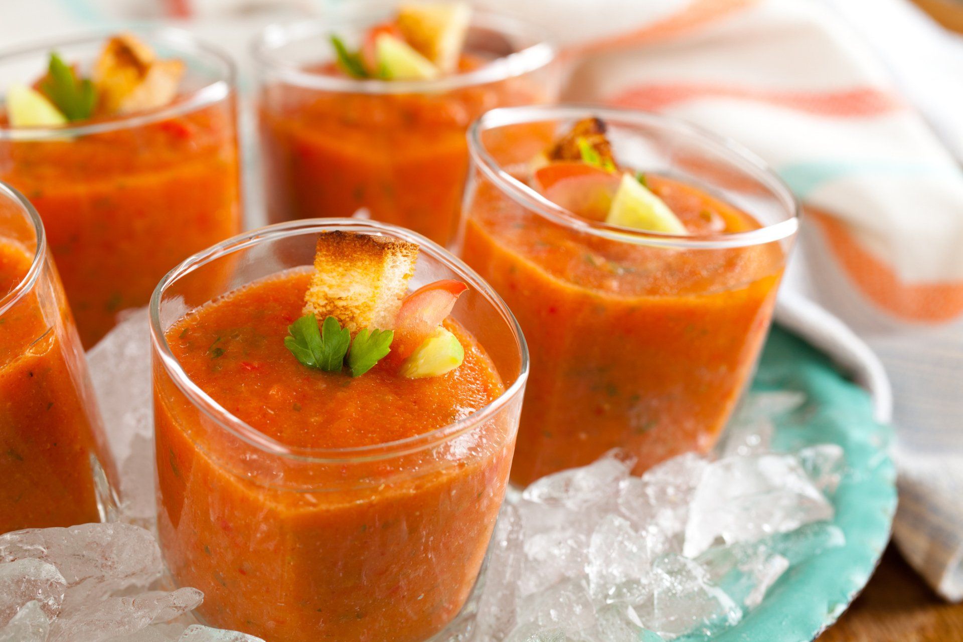 A group of glasses filled with tomato soup on ice.