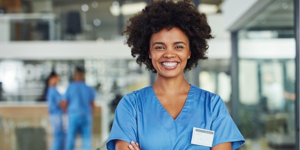 A nurse is standing in a hospital with her arms crossed and smiling.