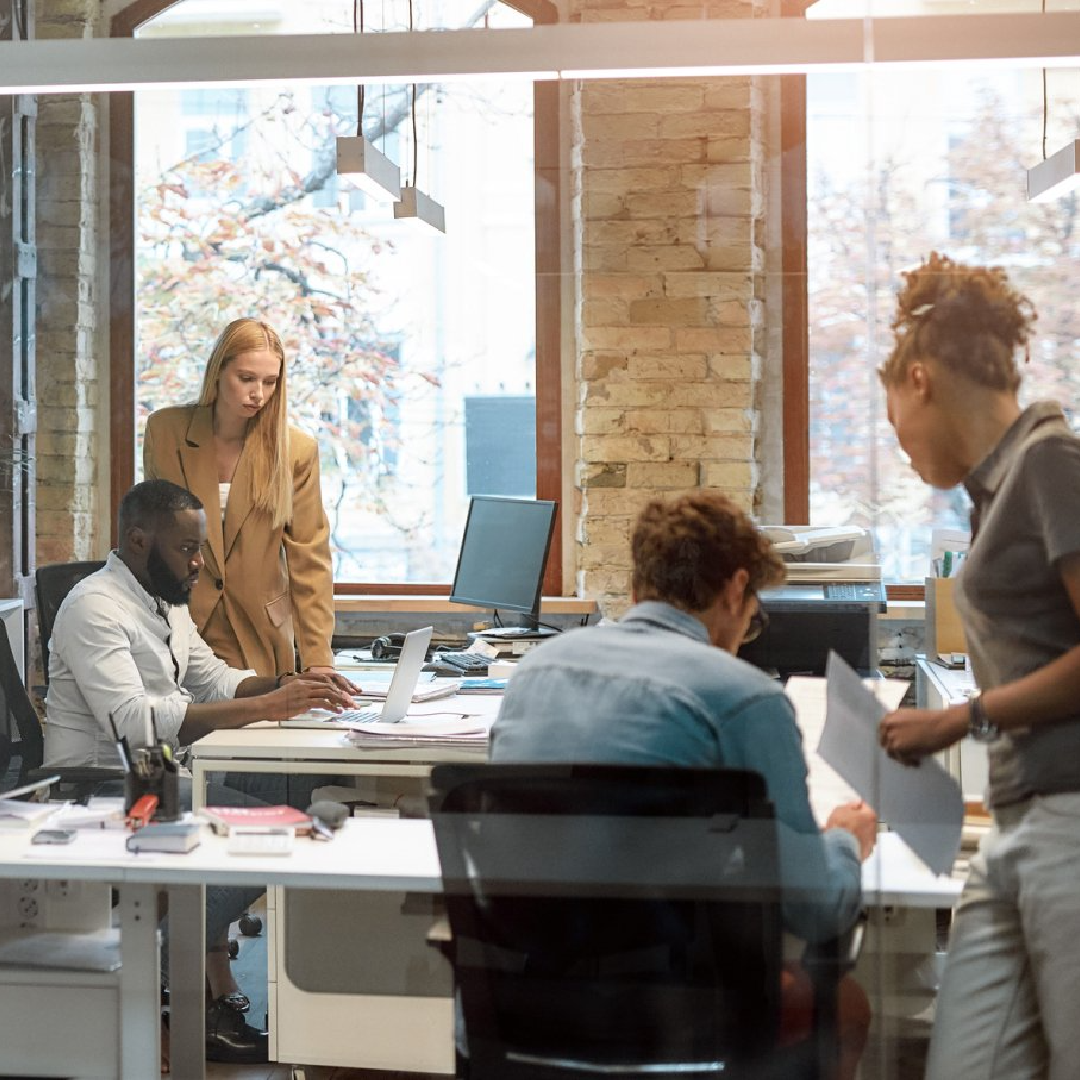 A group of people are standing around a desk in an office.